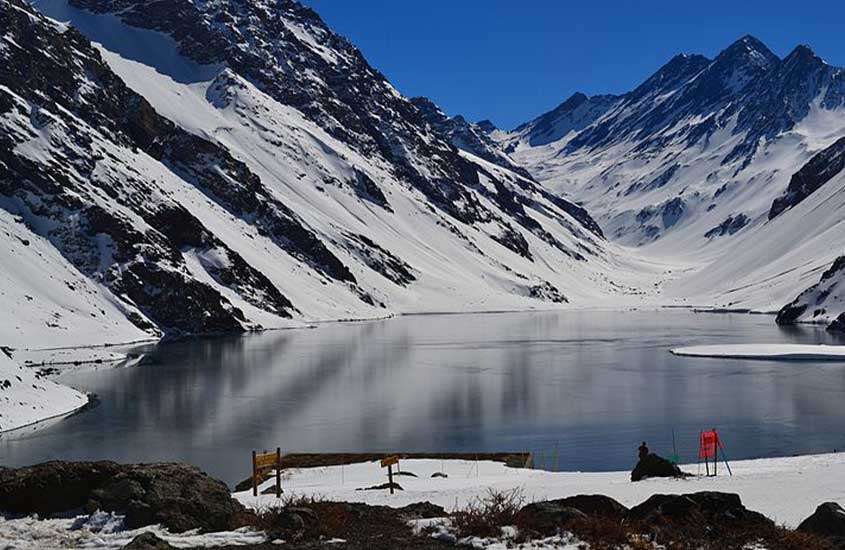 durante dia ensolarado, lago rodeado por montanhas cobertas de neve em Portillo, um dos melhores lugares para esquiar no chile