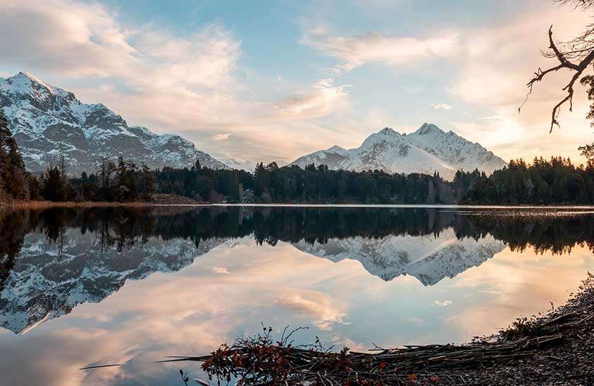 durante entardecer, montanhas cobertas de neve refletindo em lago cristalino em Bariloche