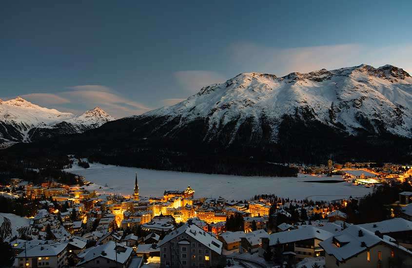 durante entardecer, vista aérea de casas em frente a montanha coberta de neve em St. Moritz.