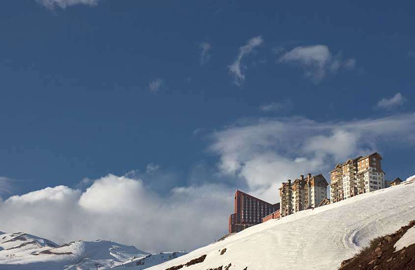 durante o dia, diversos prédios sobre montanha coberta de neve em Valle Nevado, um dos melhores lugares para esquiar na américa do sul