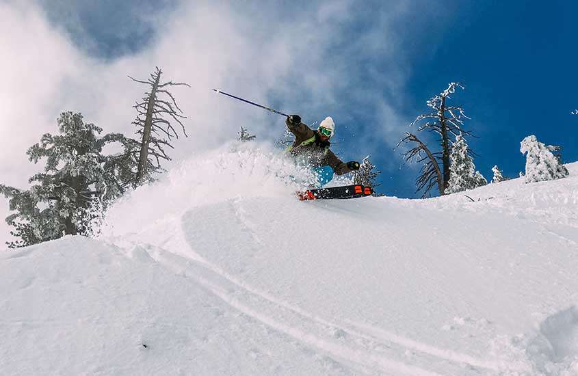 durante o dia, pessoa com touca, óculos de proteção, casaco e calça, praticando snowboard em montanha coberta de neve