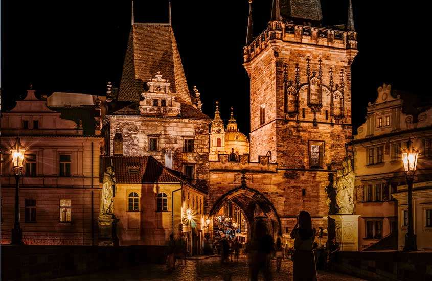 Durante a noite, pessoas caminhando em ruas de paralelepípedo cercadas por prédios históricos na Cidade Velha de praga república checa