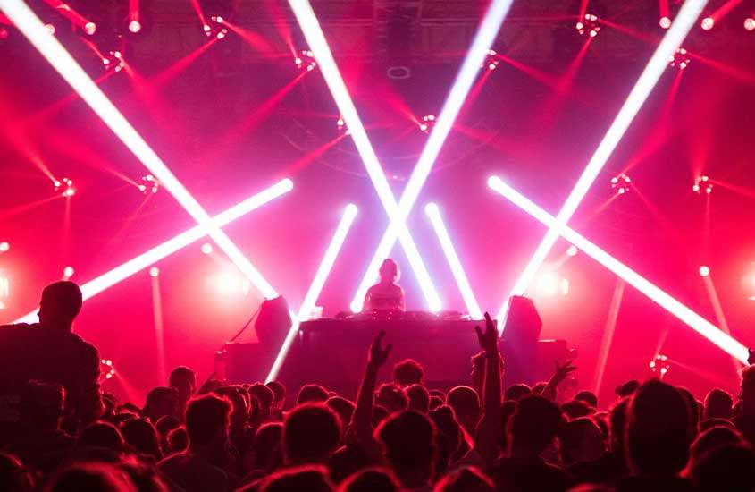 Pessoas dançando em frente à mesa de DJ em uma balada iluminada por luzes vermelhas de LED em Praga república checa