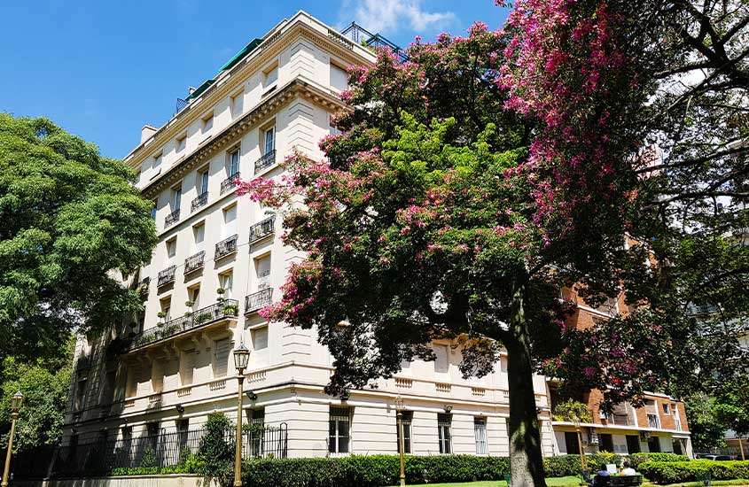Durante o dia, vista de árvores floridas em frente a um prédio em estilo parisiense em Recoleta, um lugar popular onde ficar em Buenos Aires