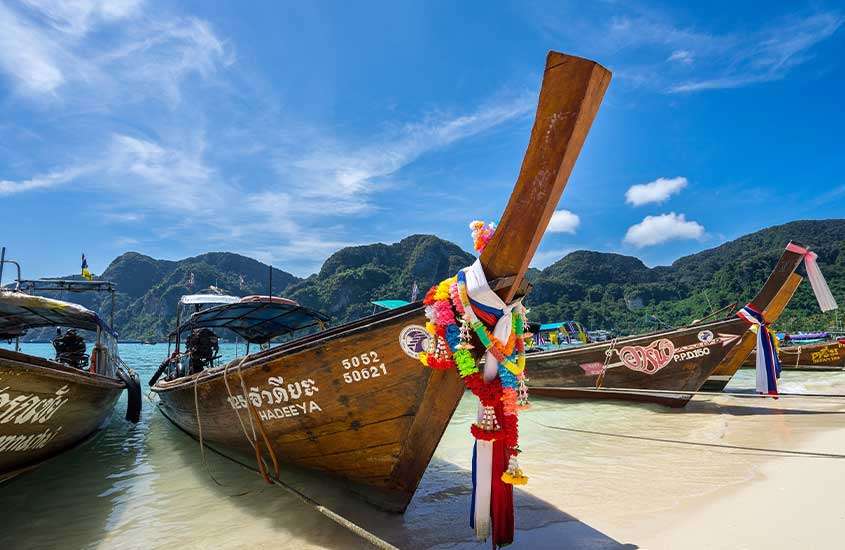 Durante um dia ensolarado, barcos tradicionais com cauda longa de madeira atracados no Tonsai Village, um lugar popular onde ficar em koh phi phi