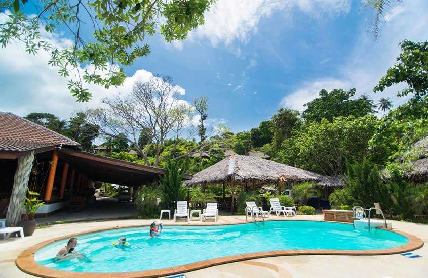 Durante o dia, três pessoas se divertindo em uma piscina com formato circular rodeada por árvores, em uma área de lazer ao ar livre de um hotel em Koh Phi Phi