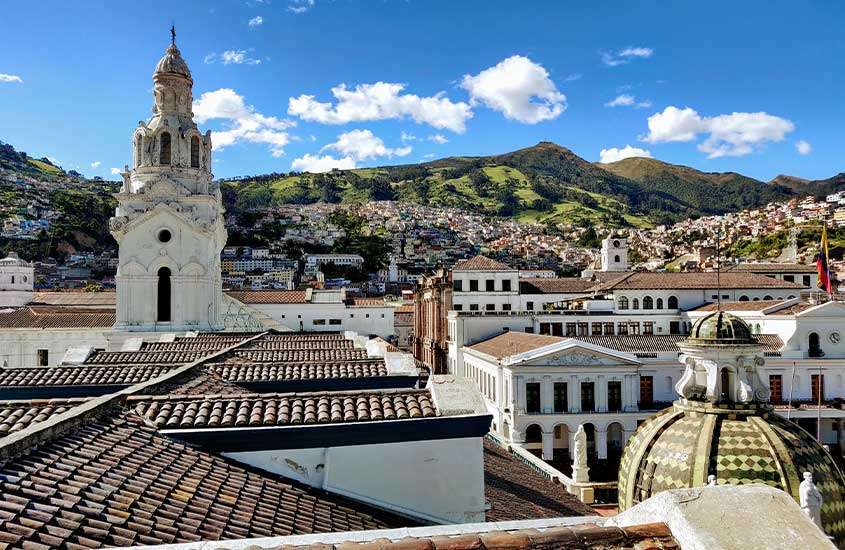 Durante o dia, vista aérea de prédios com telhados marrons em estilo colonial, rodeados por montanhas no Equador, um dos países mais seguros da américa do sul.