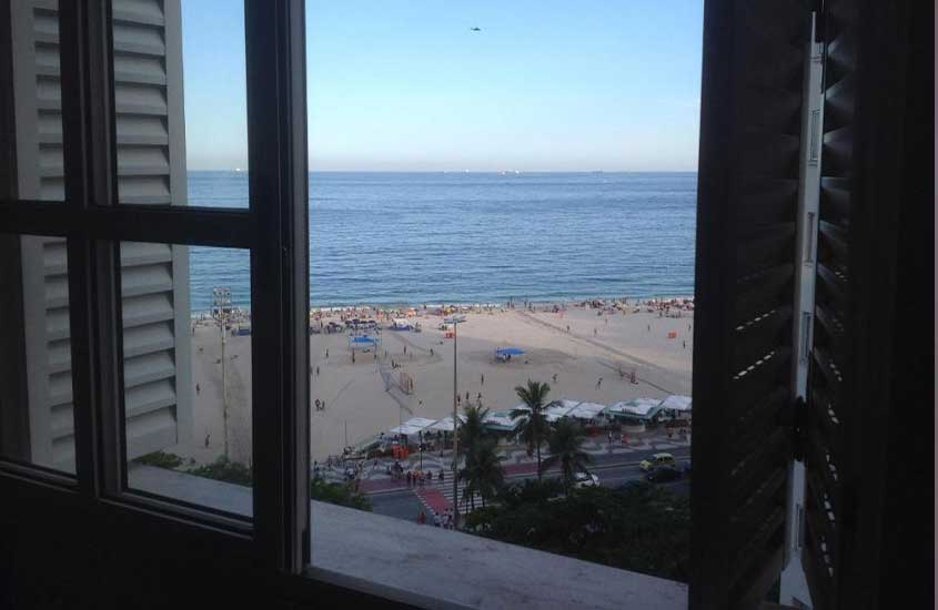 durante o dia, areia e mar de praia de copacabana, vista de janela de apartamento de temporada para passar o réveillon no rio de janeiro.