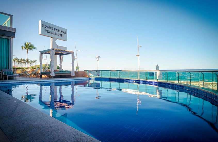 Durante o dia, espreguiçadeiras e cadeiras em frente à piscina ao ar livre em cobertura de hotel para passar réveillon em Salvador com vista para o mar.