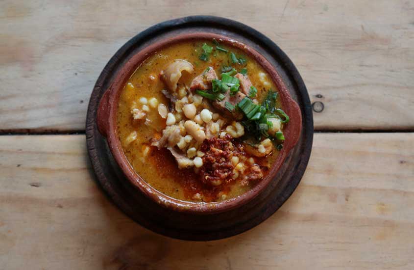 Locro, prato típico da culinária de Bariloche, servido em uma vasilha redonda sobre uma mesa de madeira