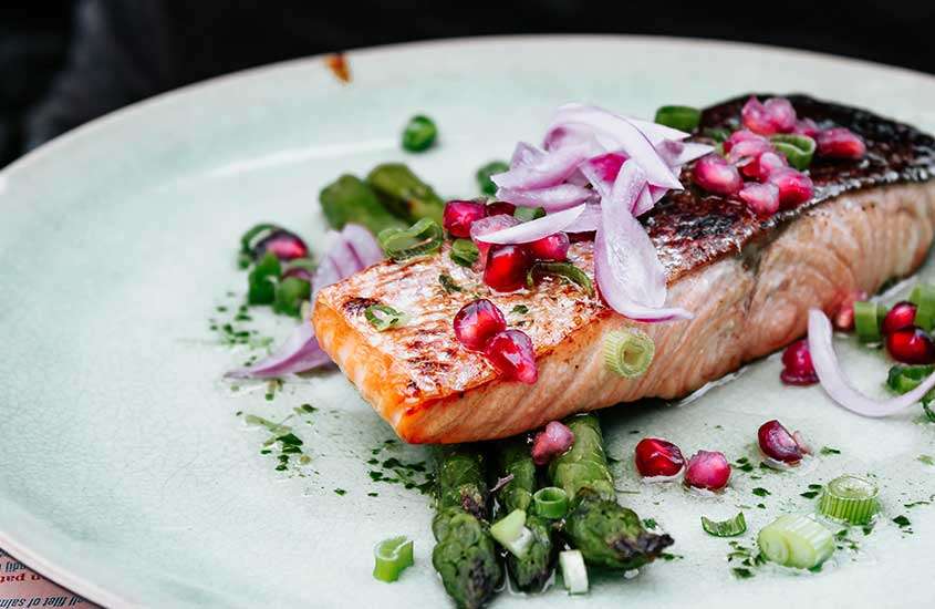 Salmão suculento acompanhado de cebola caramelizada e vagem, servido em um prato branco redondo em um restaurante em bariloche