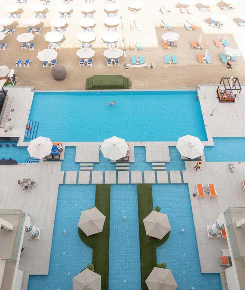 Durante o dia, vista aérea de diversas piscinas, espreguiçadeiras e guarda-sóis em área de lazer ao ar livre de um dos hotéis em dubai 5 estrelas