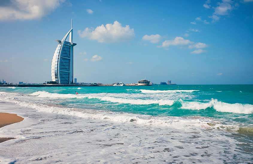 durante o dia, ondas em mar e, ao fundo, arranha-céus em Jumeirah Beach, um lugar onde ficar em dubai