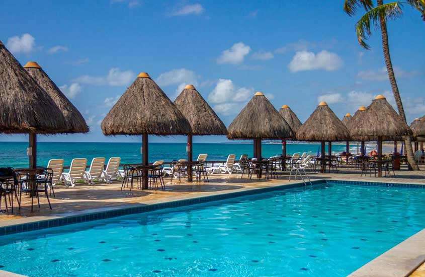 durante um dia ensolarado, espreguiçadeiras e guarda-sóis de palha em frente ao redor de piscina ao ar livre em um dos hotéis no pontal do cupe com vista para o mar