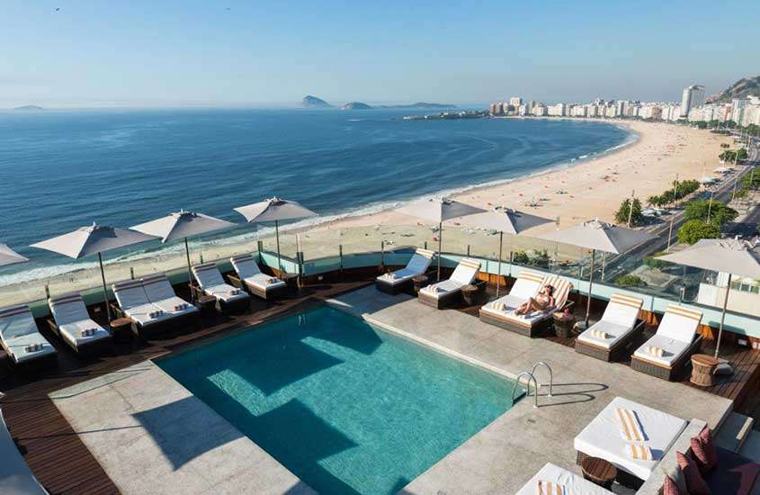 durante um dia ensolarado, vista aérea de espreguiçadeiras ao redor de piscina quadrada em cobertura de hotel em copacabana com vista para o mar