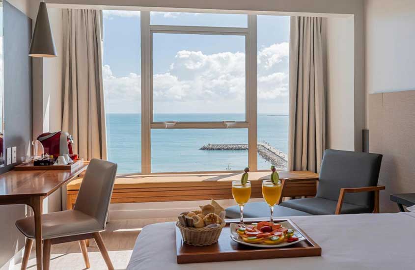Café da manhã servido em uma bandeja na cama de uma suíte de hotel com vista para o mar