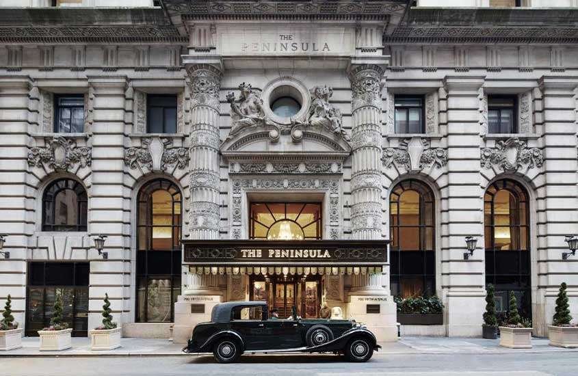 durante o dia, carro preto estacionado em frente a fachada de hotel the peninsula, um dos hotéis para o ano novo em Nova York