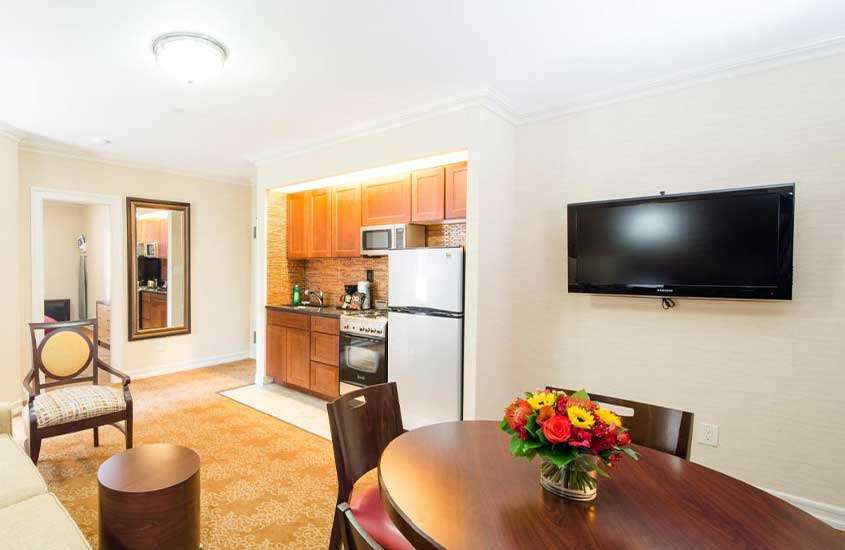 cozinha compacta com armários, fogão e geladeira, mesa de jantar e televisão em apartamento para passar o reveillon Nova York