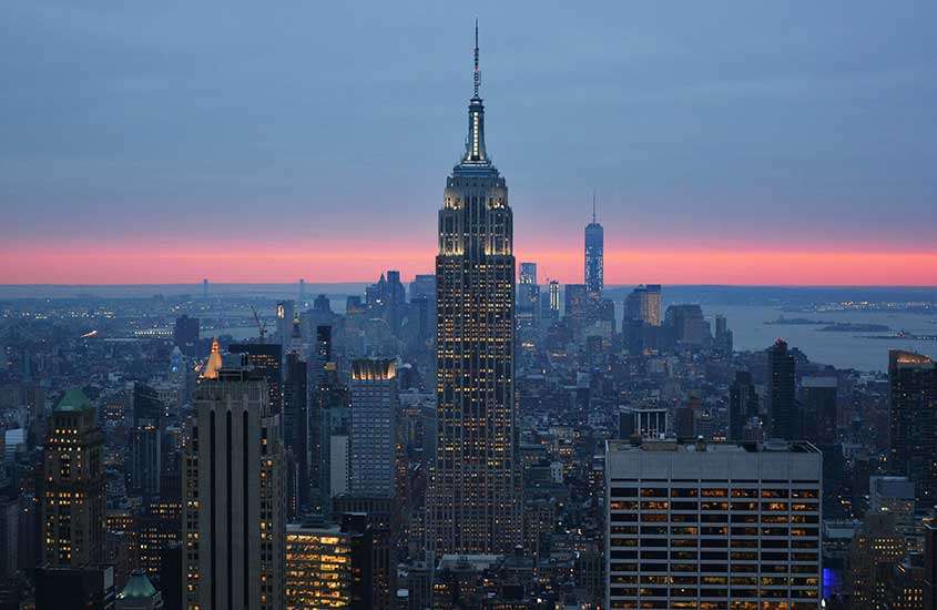 Durante o entardecer, o icônico Empire State Building e prédios ao seu redor vistos de rooftop em nova york