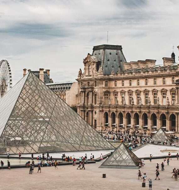 durante o dia, vista aérea de pessoas caminhando em frente à Pirâmide de Vidro no pátio do Louvre, um dos melhores museus em paris