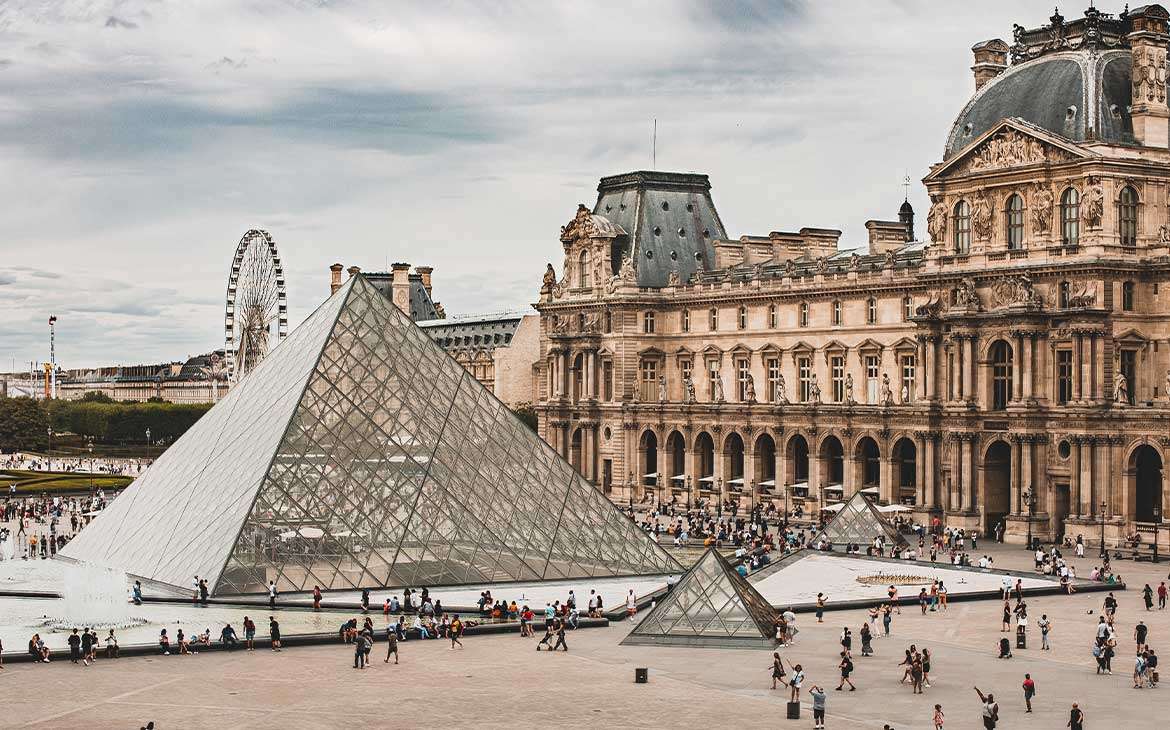 durante o dia, vista aérea de pessoas caminhando em frente à Pirâmide de Vidro no pátio do Louvre, um dos melhores museus em paris