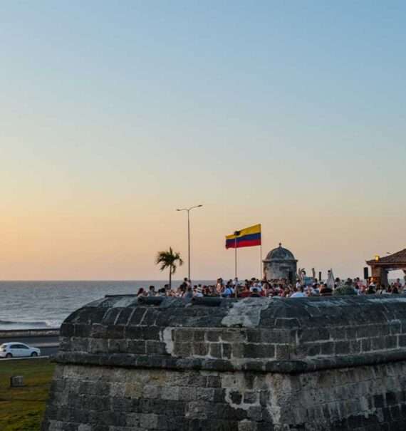 Mirante no interior da cidade murada de Cartagena, durante o entardecer, com uma animada multidão de pessoas apreciando a vista para o mar.