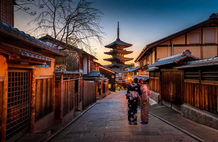 Entardecer em Kyoto, com geishas elegantemente vestidas com kimonos caminhando pelas ruas.