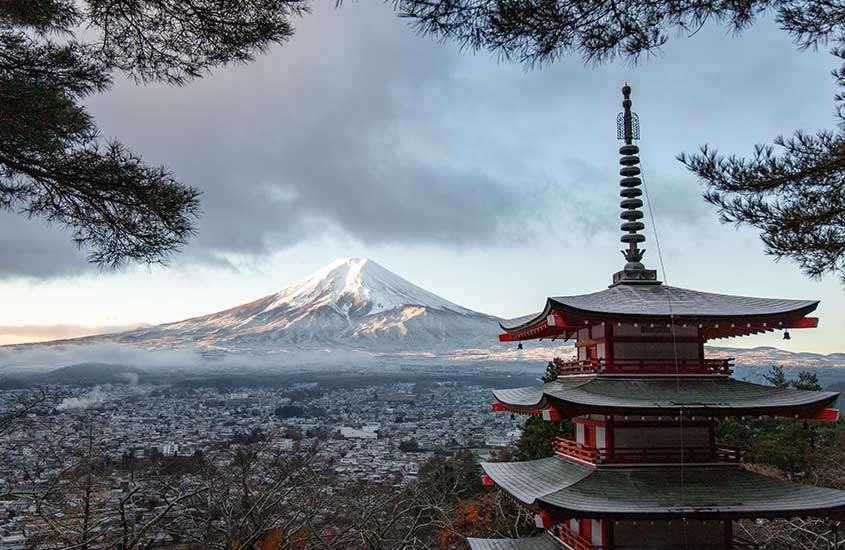 Vista aérea durante o dia de um templo com arquitetura típica japonesa, com o Monte Fuji (montanha mais alta do Japão) ao fundo.