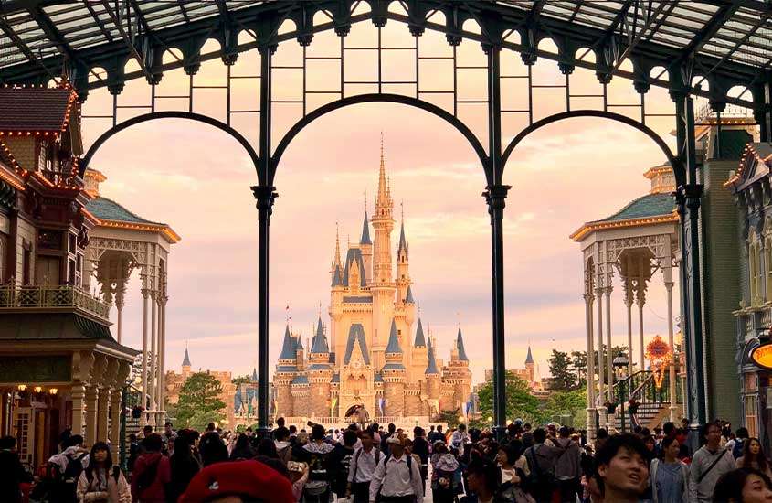 Durante o dia, diversas pessoas caminhando em Tokyo Disneyland, parque temático que é um dos lugares perto de Tokyo.