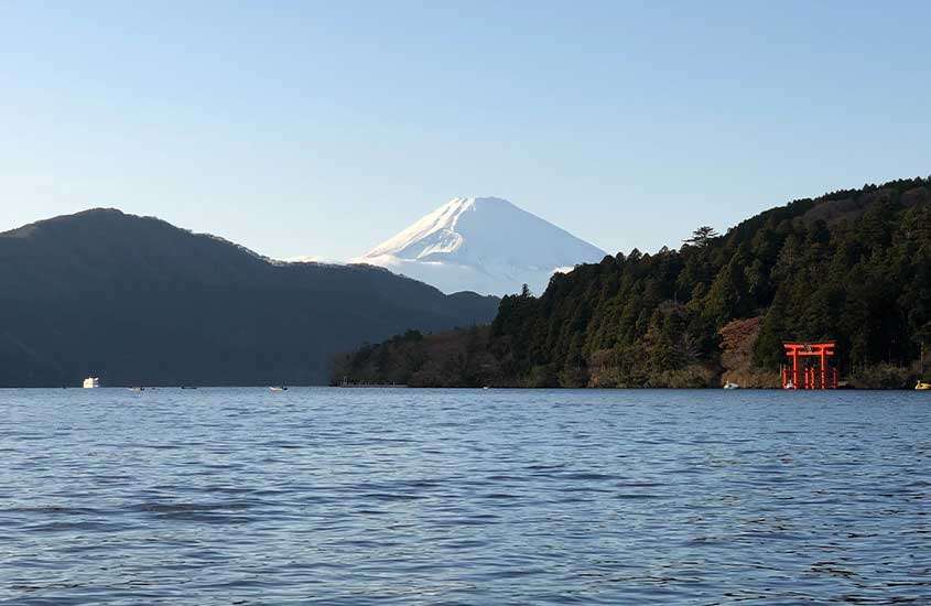 Durante um dia ensolarado, árvores ao redor de lago e, ao fundo, Monte Fuji, um dos lugares perto de Tóquio mais famosos.