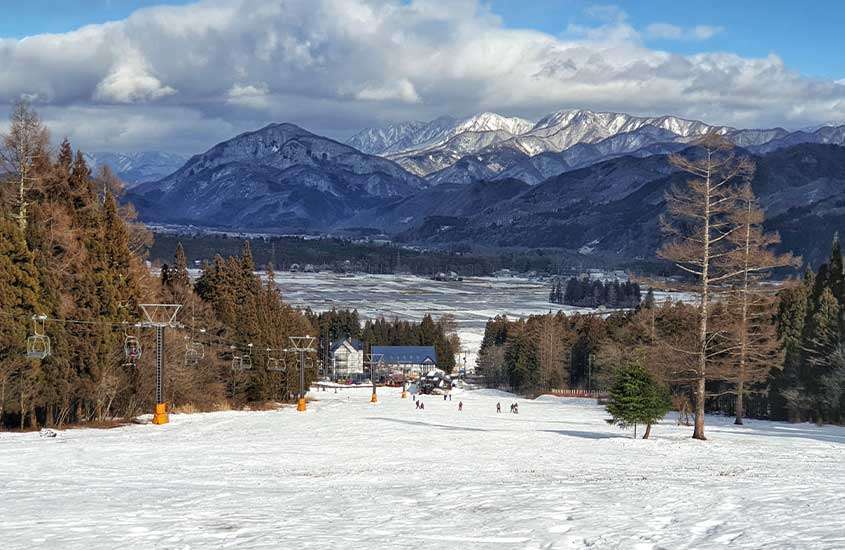 Pessoas esquiando em Nagano durante o dia, com a vista de montanhas cobertas de neve.