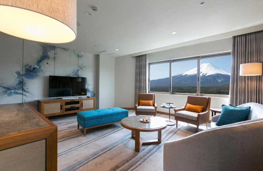 Sofás, poltronas, mesa e televisão dispostos em uma suíte de hotel com vista para o Monte Fuji durante o dia.