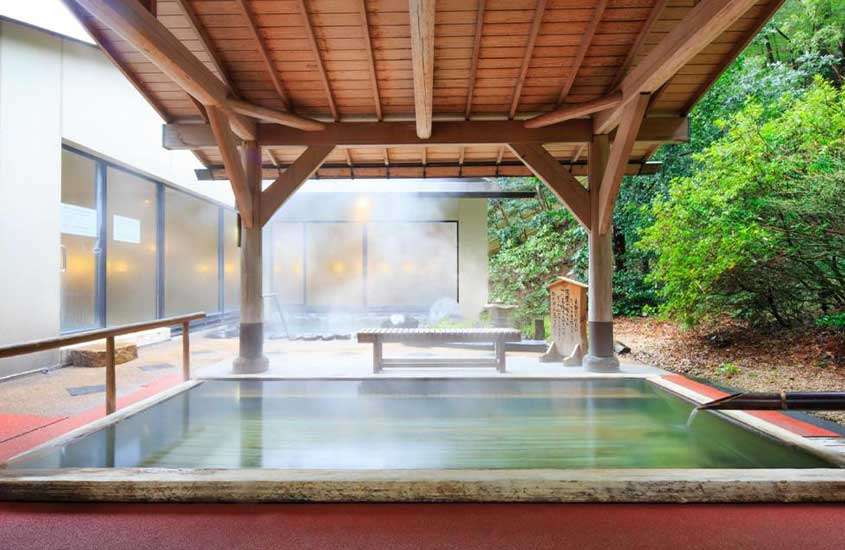 Durante o dia, piscina termal em varanda rodeada por árvores em um hotel em Hakone.