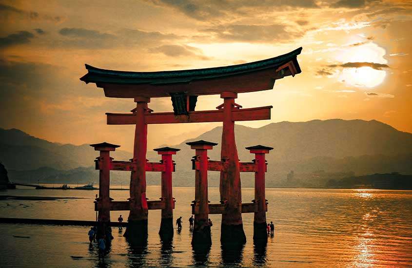 Entardecer no mar de Miyajima, com um torii flutuante, um icônico portão japonês, refletindo na água.