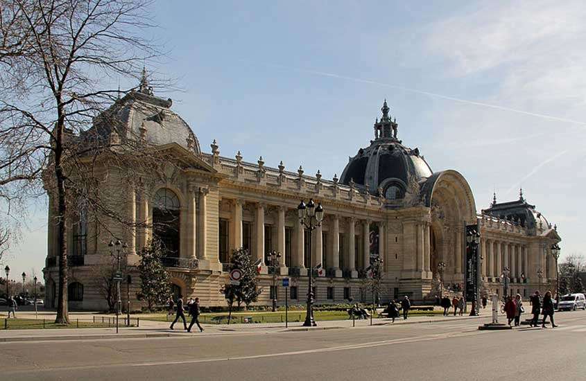 durante um dia ensolarado, pessoas caminhando em frente a prédio em estilo Beaux-Arts, com um cúpula charmosa, onde funciona o Petit Palais, um museu de paris