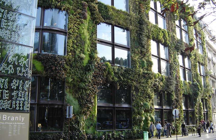 durante o dia, pessoas caminhando em frente a fachada de prédio coberta de plantas, onde funciona um museu em paris