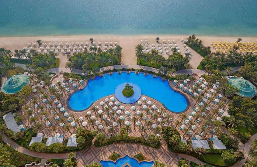 durante um dia ensolarado, vista aérea de árvores ao redor de piscina em hotel em Dubai em frente ao mar