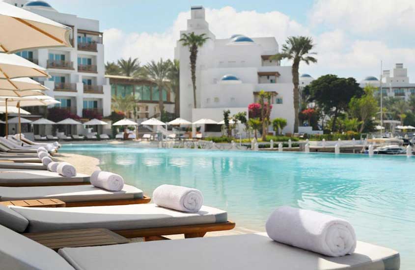 durante um dia ensolarado, toalhas brancas em cima de diversas espreguiçadeiras ao redor de piscina ao ar livre em um dos melhores hotéis em dubai