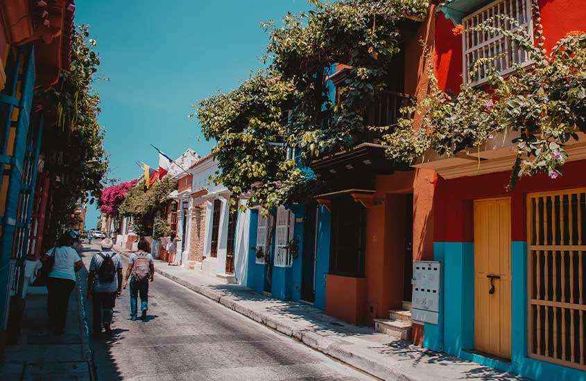 Durante um dia ensolarado, pessoas caminham em uma rua arborizada e encantadora, cercada por casas coloridas em San Diego, um lugar onde ficar em Cartagena das índias.
