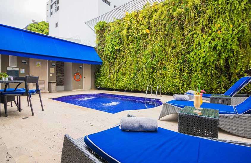 Durante o dia, espreguiçadeiras azuis em frente a pequena piscina em área de lazer ao ar livre de um dos melhores hotéis próximos ao aeroporto de Cartagena.