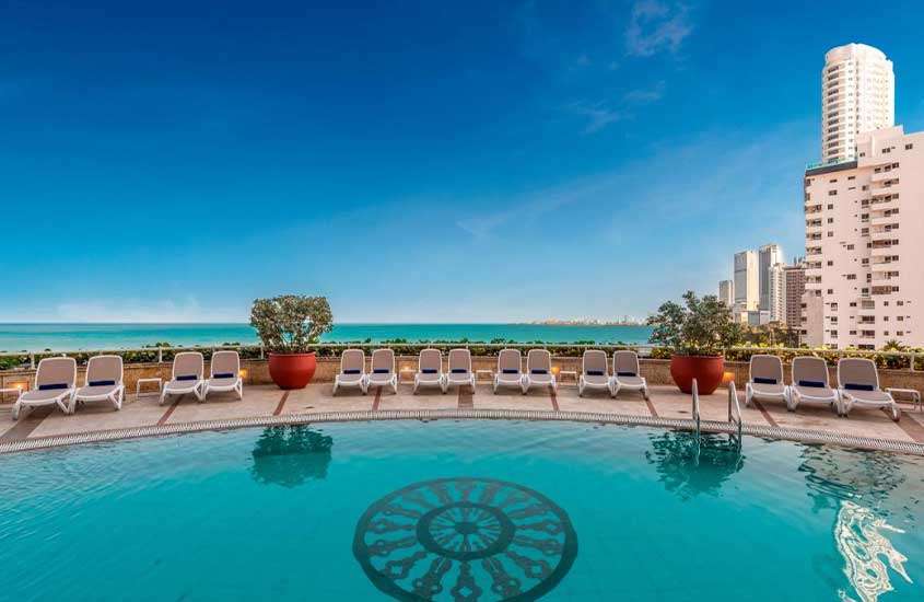 Durante um dia ensolarado, espreguiçadeiras e vasos de plantas em frente a piscina em cobertura de hotel com vista para o mar.