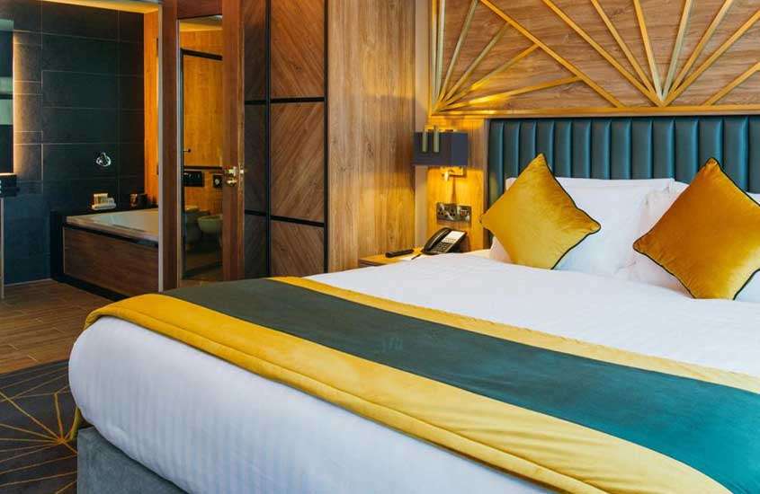banheira de hidromassagem e cama de casal em suíte de hotel com revestimentos e piso de madeira