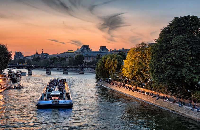durante um entardecer, vista panorâmica de pessoas em cruzeiro pelo rio sena, um dos melhores passeios em paris