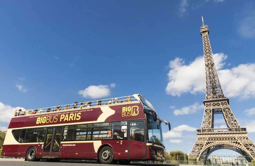 durante o dia, ônibus vermelho de dois andares passando em frente a Torre Eiffel
