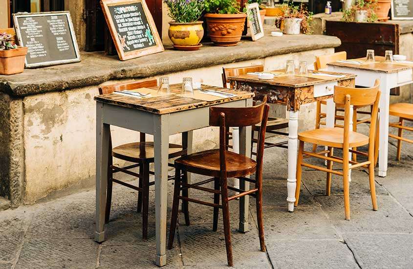 Vista de um restaurante rústico, com mesas e cadeiras dispostas em um ambiente acolhedor, decorado com chão de pedra e plantas