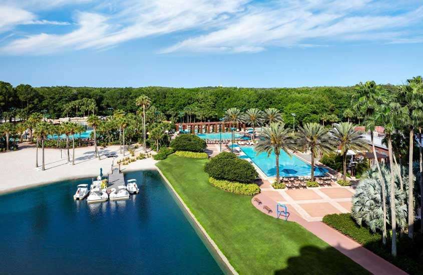 durante um dia ensolarado, vista aérea de praia privativa e piscina ao livre em complexo de lazer de um dos hotéis disney orlando, rodeado por árvores.