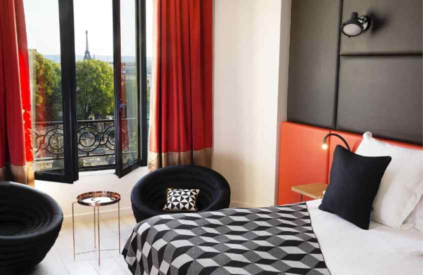 Quarto de luxo de um hotel com janela acortinada, cama de casal, mesas e poltronas