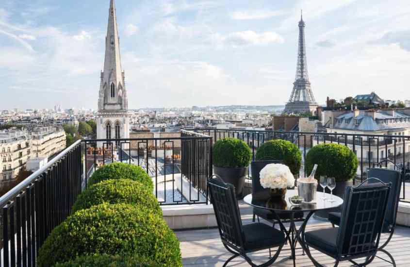 Em um dia de sol, cobertura de um hotel em Paris com vista para a Torre com mesas, cadeiras, plantas ao redor e paisagem da cidade