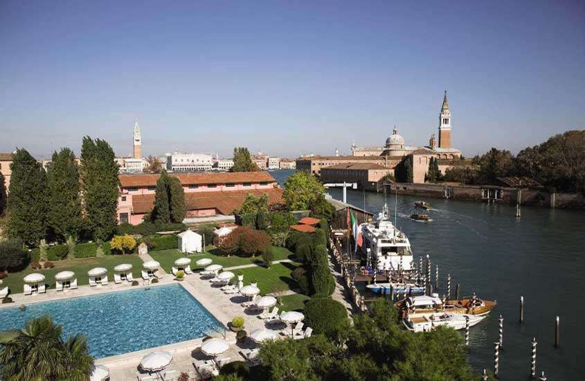 durante o dia, vista aérea de árvores, espreguiçadeiras e guarda-sóis ao redor de grande piscina retangular em hotel em Veneza com vistas para a lagoa