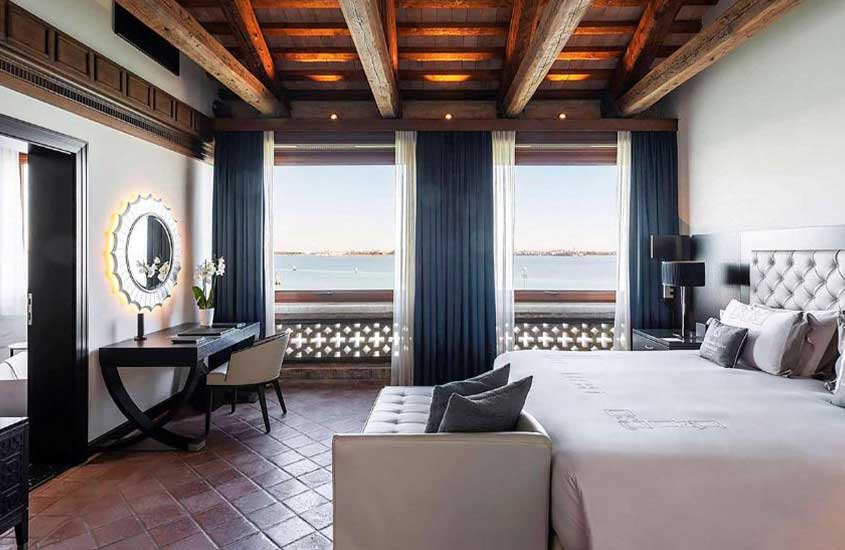 Durante o dia, mesa de escritório, sofá e cama de casa em suíte de hotel em Veneza com vista para uma lagoa.